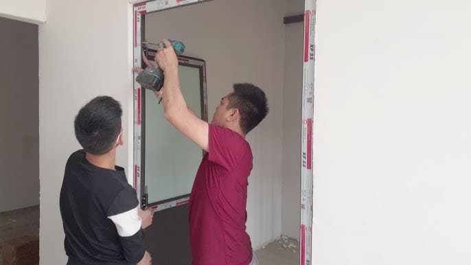 Thợ xây dùng máy khoan búa SDS Max và mũi khoan tường để khoan lỗ cố định khung cửa vào tường bê tông.
